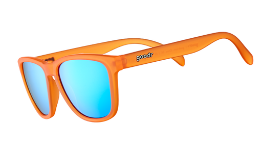Vue de trois quarts d'angle de lunettes de soleil translucides orange vif avec des verres réfléchissants bleus sur un fond blanc.