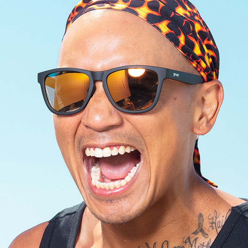 Un homme portant un durag à motifs de flammes et des lunettes de soleil noires avec des verres réfléchissants ambrés s'écrie joyeusement.