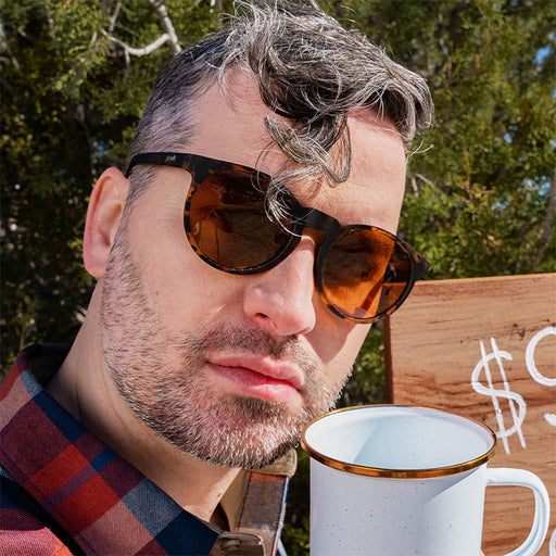 Un barista hipster regarde d'un œil critique devant lui en portant des lunettes de soleil en écaille marron avec des verres non réfléchissants marron.