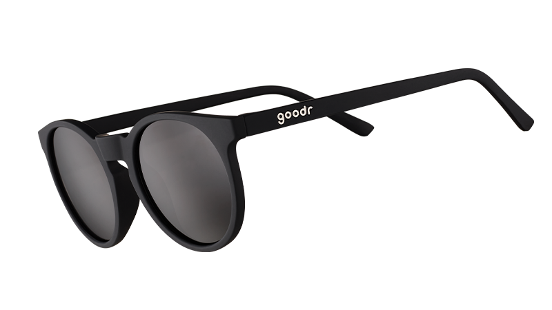 Vue de trois quarts d'angle de lunettes de soleil rondes noires d'inspiration rétro avec des verres noirs non réfléchissants.