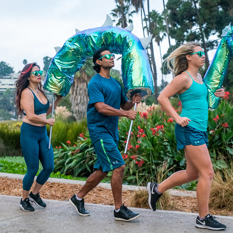 Trois coureurs portant des lunettes de soleil aux verres sarcelle tiennent des sections d'une marionnette géante du monstre du Loch Ness alors qu'ils font leur jogging.