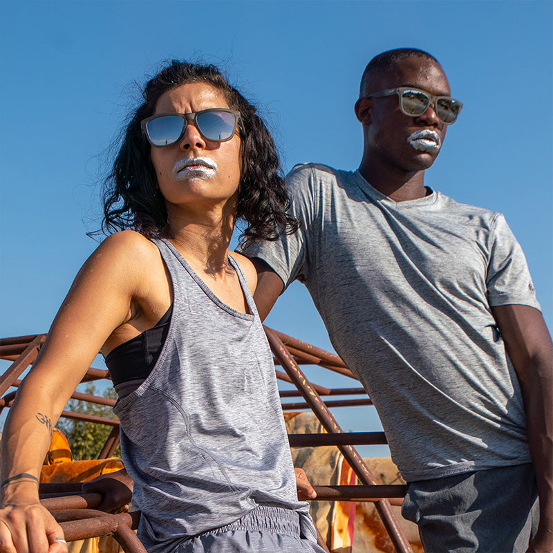 Un homme et une femme portant des lunettes de soleil grises avec des verres gris et de la peinture argentée sur la bouche regardent au loin avec férocité.