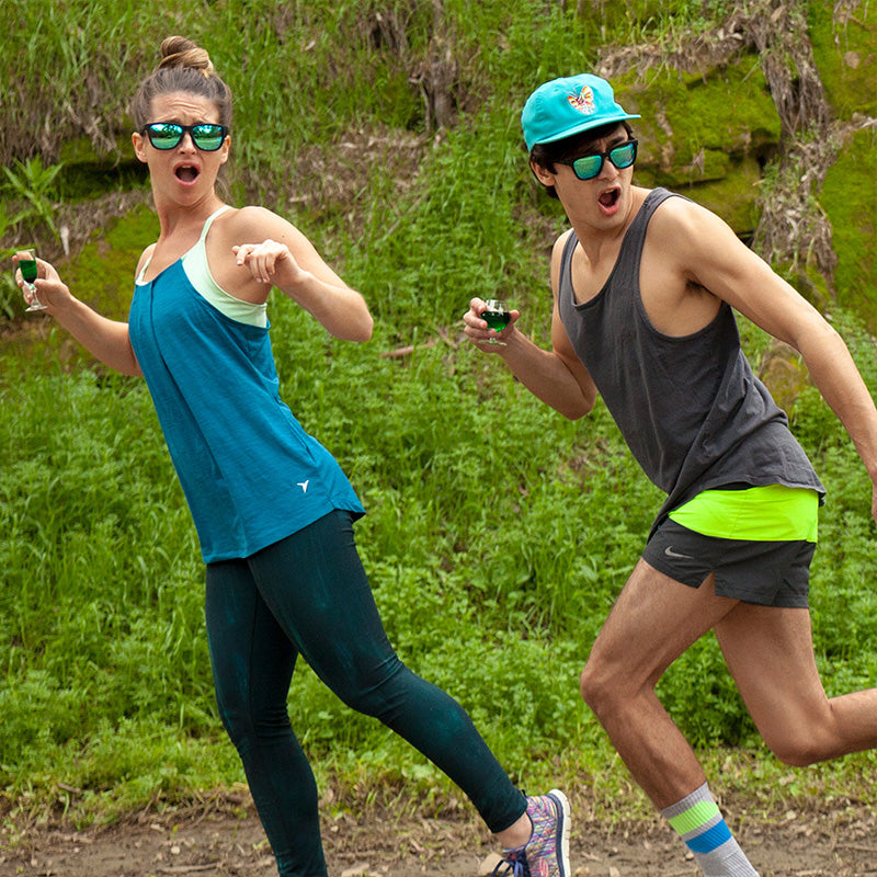 Deux coureurs portant des lunettes de soleil noires avec des verres réfléchissants verts regardent par-dessus leurs épaules, effrayés, alors qu'ils font leur jogging dans une prairie.