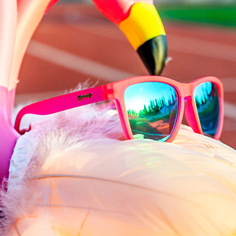 Vue de trois quarts d'angle de lunettes de soleil roses avec des verres réfléchissants verts posées sur un flotteur de piscine gonflable en forme de flamant rose.