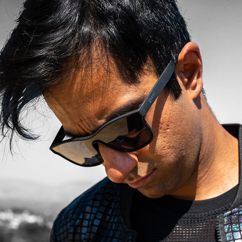 Un homme portant des lunettes de soleil noires à verres simples regarde sur le côté, déterminé.